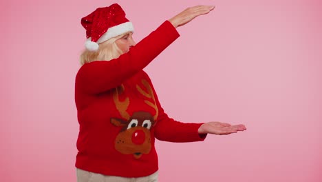 Grandmother-in-Christmas-deer-sweater-showing-thumbs-up-and-pointing-at-on-blank-advertisement-space
