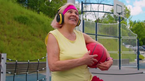Ältere-Frau-Großmutter-Nach-Dem-Sport-Basketball-Training-Sitzen-Und-Musik-Auf-Dem-Spielplatz-Hören