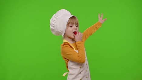 Child-girl-dressed-as-cook-chef-baker-in-apron-eats-delicious-fresh-strawberries-and-dances