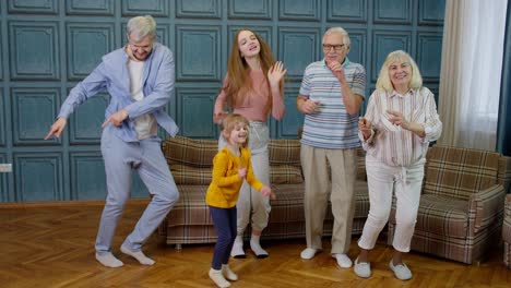 Family-members-of-different-generations-having-fun-listening-music,-dancing-crazy-in-room-at-home