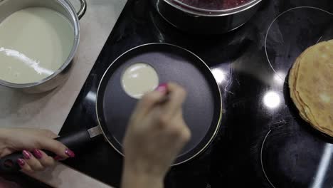 The-process-of-cooking-homemade-pancakes.-Woman-pours-pancake-dough-on-pan