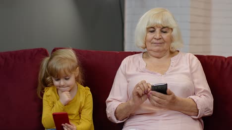 Senior-grandmother-with-child-girl-granddaughter-using-digital-mobile-phone,-playing-games-at-home