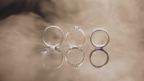 Wedding-and-engagement-rings-lying-on-dark-water-surface-shining-with-light