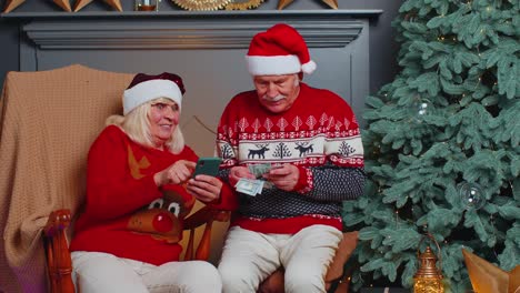 Senior-family-couple-searching-purchase-online-Christmas-gifts-in-mobile-phone-application-at-home