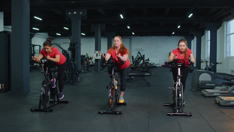 Healthy-Caucasian-group-of-women-exercising-workout-on-stationary-cycling-machine-bike-in-gym
