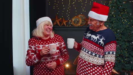 Senior-old-wife-and-husband-talking,-drinking-tea-near-glowing-xmas-tree-on-Christmas-in-home-room