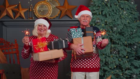 Smiling-married-senior-grandparents-man-woman-holding-Christmas-gift-boxes-and-bengali-sparkles