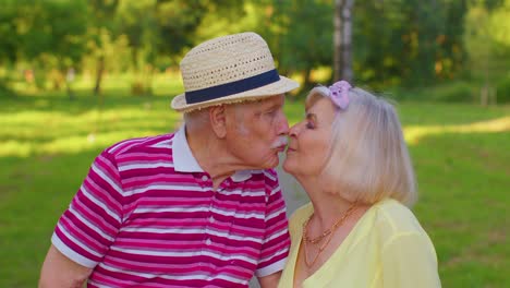 Senior-old-stylish-tourists-couple-grandmother,-grandfather-walking-in-summer-park-and-making-a-kiss