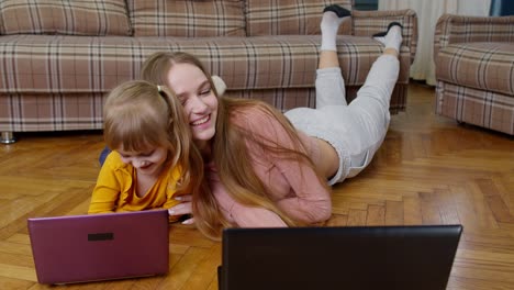 Woman-nanny-and-child-girl-studying-together-with-computer-laptop,-while-lying-on-warm-floor-at-home