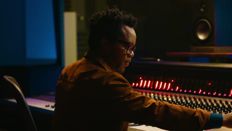 Portrait-of-african-american-audio-technician-uses-mixing-console-with-knobs