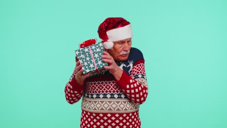Senior-grandfather-man-in-Christmas-sweater-received-present,-interested-in-what-inside-gift-box