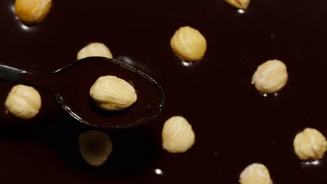 Melted-liquid-dark-chocolate-and-hazelnuts-rotating,-process-of-making-sweet-desserts-with-nuts