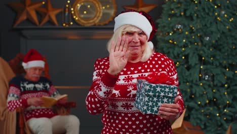 Senior-grandmother-in-Christmas-sweater-smiling-friendly-at-camera-and-waving-hands-gesturing-hello