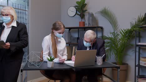 Elderly-man-boss-with-woman-secretary-in-medical-mask-working-in-office-during-coronavirus-pandemic