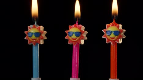 Birthday-festive-candles-in-form-of-sun-in-sunglasses-turning,-spinning-isolated-on-black-background