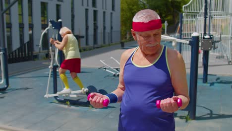 Senior-man-grandfather-doing-active-training-weightlifting-exercising-with-dumbbell-on-playground