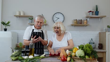 Senior-couple-cooking-salad-with-vegetables.-Woman-dancing-holding-fresh-slices-of-pepper-on-eyes