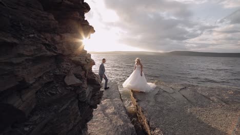 Groom-goes-to-bride-and-gives-her-a-hand.-Newlyweds-on-mountainside-by-the-sea