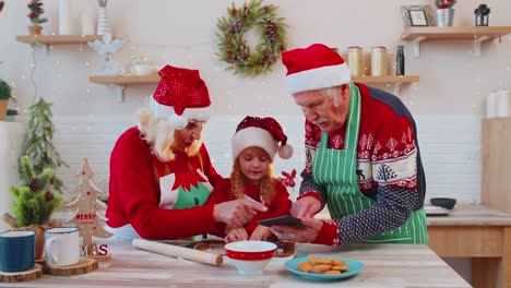 Senior-grandparents-and-grandchild-watching-cooking-lesson-using-digital-tablet-at-Christmas-kitchen