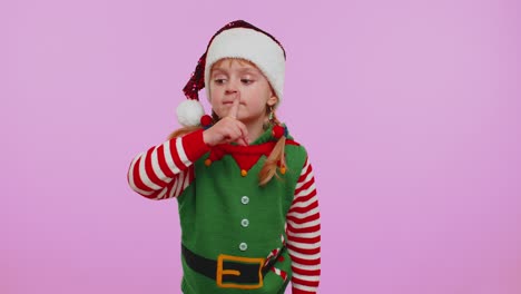 Child-girl-in-Christmas-Elf-costume-presses-index-finger-to-lips-makes-silence-gesture-sign,-secret