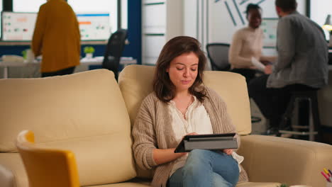 Employee-taking-break-sitting-on-confortable-couch-holding-tablet-browsing