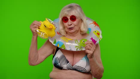 Senior-woman-tourist-in-sunglasses-dancing,-playing-with-inflatable-duck-toy,-rubber-swimming-ring