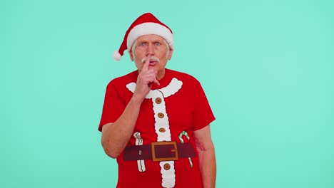 Senior-old-man-in-Christmas-t-shirt-presses-index-finger-to-lips-makes-silence-gesture-sign,-secret