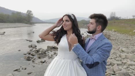 Wedding-couple-standing-near-mountain-river.-Groom-and-bride-in-love