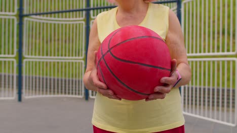 Senior-woman-grandmother-athlete-posing-playing-with-ball-outdoors-on-basketball-playground-court