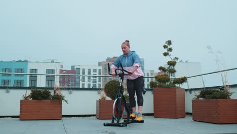 Gesunde-Kaukasische-Frau,-Die-Training-Auf-Einem-Stationären-Fahrrad-Im-Fitnessstudio-Auf-Dem-Dach-Des-Hauses-Durchführt