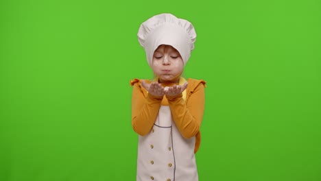 Child-girl-kid-dressed-as-professional-cook-chef-blowing-flour-from-hands-into-camera-on-chroma-key