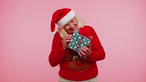Senior-grandmother-woman-in-Christmas-sweater-received-present,-interested-in-what-inside-gift-box