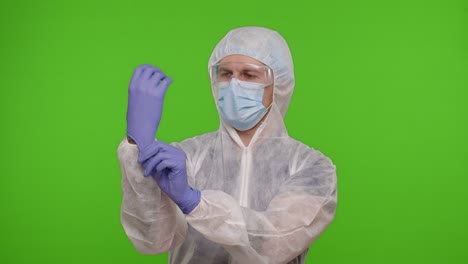 Young-healthcare-worker-doctor-standing-on-chroma-key-and-puts-on-hand-gloves,-coronavirus-pandemic