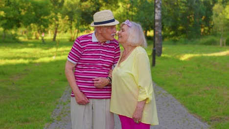 Senior-old-stylish-tourists-couple-grandmother,-grandfather-walking-in-summer-park-and-making-a-kiss