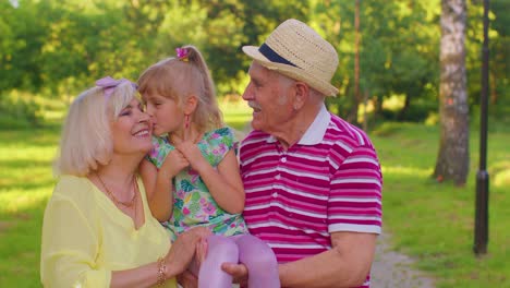 Little-cute-granddaughter-child-embracing-with-her-grandmother-and-grandfather-family-couple-in-park