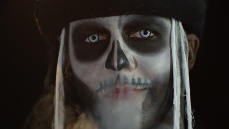 Creepy-man-with-skeleton-makeup-exhaling-cigarette-smoke-from-his-mouth-and-nose,-smiling