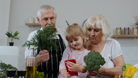 Blogger-grandchild-girl-making-selfie-on-phone-with-senior-grandparents-at-kitchen-with-vegetables