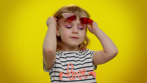 Funny-playful-blonde-kid-child-wearing-sunglasses,-blinking-eye,-looking-with-charming-smile