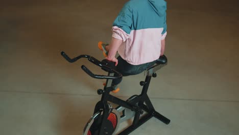 Sportliches-Mädchen-Macht-Akrobatische-Tricks-Auf-Dem-Fahrrad-Und-Trainiert-Auf-Einem-Stationären-Fahrradgerät-Im-Innenbereich