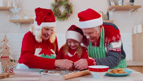 Senior-family-grandparents-with-granddaughter-in-Santa-Claus-hats-preparing,-cooking-homemade-cookie