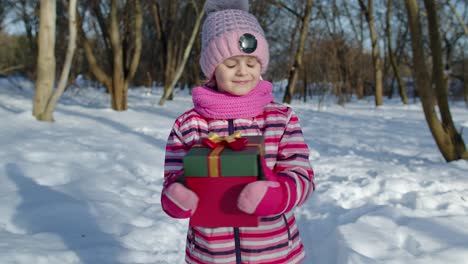 Joyful-little-smiling-kid-girl-holding-Christmas-present-gift-box-in-winter-park,-xmas-eve-holidays