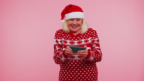 Besorgte-Großmutter-Im-Weihnachtspullover-Spielt-Begeistert-Rennvideospiele-Auf-Dem-Handy