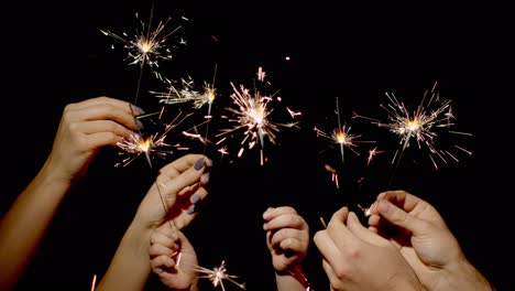 Close-up-of-hands-holding-and-waving-bengal-fire-burning-sparklers-in-front-of-black-background