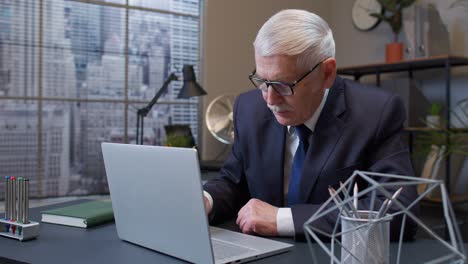 Concentrated-senior-business-man-using-laptop-sits-at-office-desk-workplace-web-designer-online-work