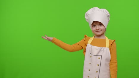 Child-girl-dressed-like-chef-cook-pointing-at-left-on-blank-space,-place-for-your-advertisement-logo