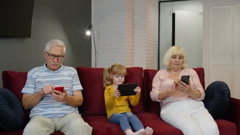 Senior-couple-grandparents-with-child-girl-granddaughter-using-digital-tablet,-mobile-phone