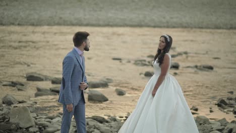 Wedding-couple-standing-near-mountain-river.-Groom-and-bride-making-faces