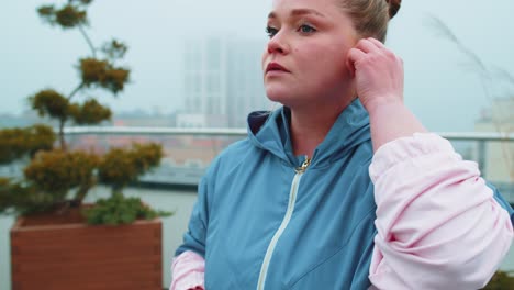 Sport-fitness-woman-wears-wireless-earphones-in-start-of-her-workout-training-on-roof-of-house