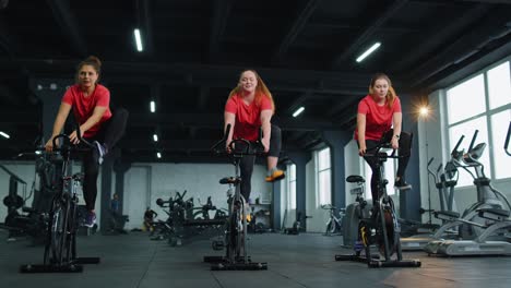 Gesunde-Kaukasische-Gruppe-Von-Frauen-Trainieren-Auf-Einem-Stationären-Fahrrad-Im-Fitnessstudio