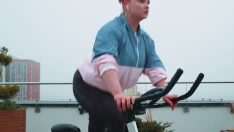 Athletic-woman-riding-on-spinning-stationary-bike-training-routine-on-house-rooftop,-weight-loss